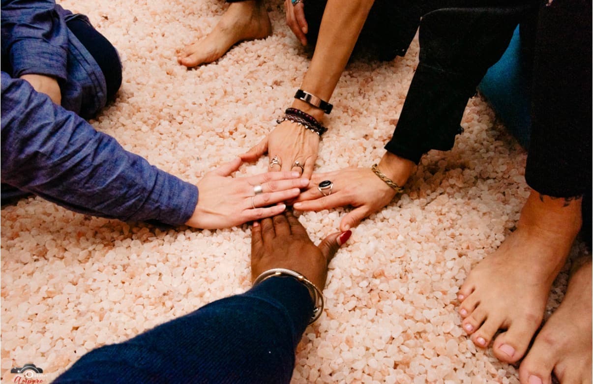 Group hands stacked together in a circle of care, resting on pink Himalayan salt stones; client-selected for the mission statement section (source: Collective healing.jpg)